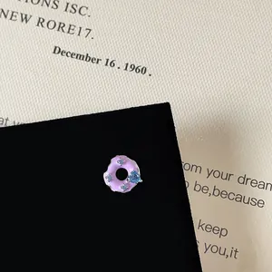 Detail of purple donut enamel stud earring with blue zircon heart on black card