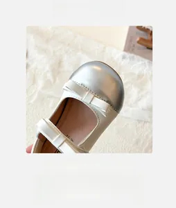 Detail of girls Mary Jane shoes with silver metallic toe cap and bow on lace background
