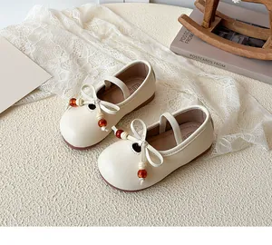 Detail of girls' cream Mary Jane shoes featuring a beaded bow and elastic strap