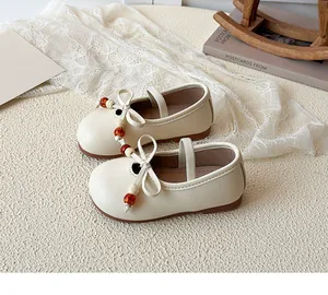 Close-up of cream Mary Jane girl shoes featuring elegant bows and orange bead accents
