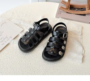 Detail shot of black kids roman sandals featuring retro metal buckles on textured white desk