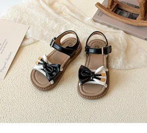 Detail of girls' black and white sandals featuring a stylish bow and gold accents