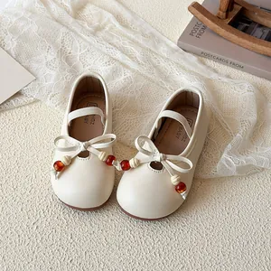 Beige Mary Jane shoes for girls with bow and beaded detail on cream lace background