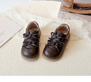 Détail de chaussures Mary Jane marron foncé avec doubles nœuds et bords festonnés pour fille