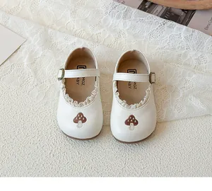 Detail der gestickten Pilze und Spitzenverzierung an weißen Kinder Mary Janes