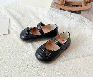 Detail von Mädchen Mary Janes in Schwarz mit Schleife und Wellenrand auf weißer Spitze