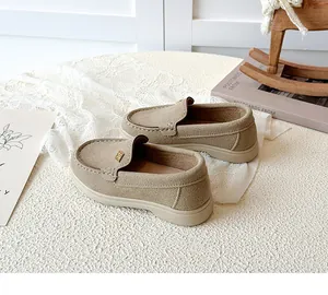 Close-up of beige suede kids loafers featuring a golden metal buckle and soft rubber sole