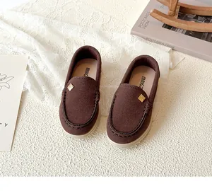 Detail of dark brown suede kids loafers featuring a decorative metal buckle and soft rubber sole