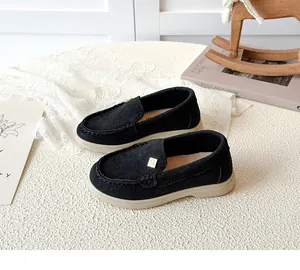 Detail of kids black suede loafers featuring a square gold buckle and soft cream soles