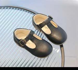 Détail de chaussures T-strap noir mat pour bébés avec boucles en bronze sur un plateau