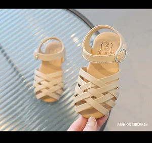 Dettaglio di sandali intrecciati beige per bambina con cinturini incrociati e fibbia in metallo