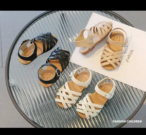 Dettaglio dei sandali intrecciati da bambina in nero, bianco e beige con fibbia