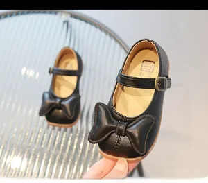 Detail of girls' black Mary Jane leather shoes featuring a large bow and buckle strap