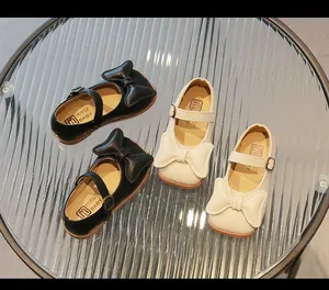 Detail of big bows and buckle straps on black and beige girls' Mary Jane shoes