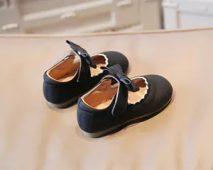 Detailed view of black Mary Jane shoes featuring a bow and scalloped edge detail