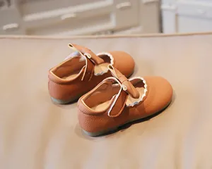 Close-up of girl's tan Mary Jane shoes featuring scalloped edges and a decorative bow