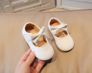 Detail of baby girls white Mary Jane shoes with bow and scalloped edge design