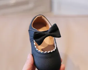 Close-up of black leather Mary Jane shoes with white scalloped trim and bow detail