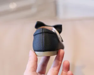 Detail of baby girl black leather shoes showing heel stitching and textured bow detail