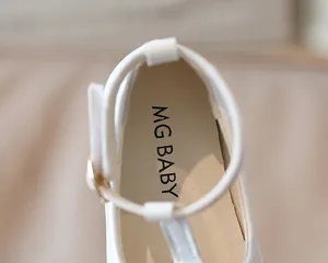 Dettaglio di scarpe in pelle bianca per bambini con cinturino a T e suola interna morbida