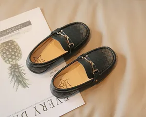 Détail de mocassins tressés noirs pour enfants avec boucle dorée posés sur magazine