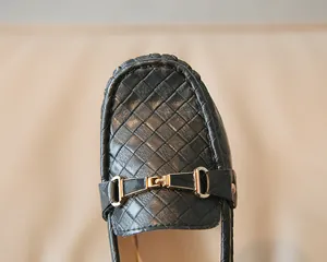 Détail de mocassins en cuir tressé noir avec une boucle décorative en émail doré