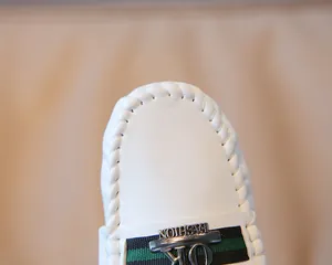 Detail eines weißen Leder-Loafers mit grün-schwarzem Webband und silberner Fashion-Schnalle