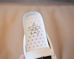 Detail eines weißen Kinder-Loafers aus Leder mit grün-rotem Streifen und Metallgebiss