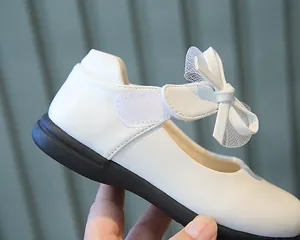 Detail of white girls' Mary Jane shoes featuring a lace bow and glossy finish