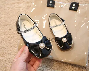 Détail de chaussures Mary Jane en cuir verni noir avec nœud perlé et bride strassée