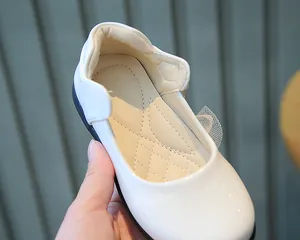 Detail of white girls Mary Jane shoes featuring glossy leather and lace bow decoration