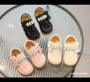Detail view of girls' patent leather shoes with pearl strap and bow on glass surface