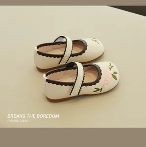 Macro detail of floral embroidery and brown scalloped trim on cream Mary Jane shoes
