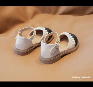 Dettaglio di scarpe Mary Jane beige da bambina con cinturino di perle e punta nera