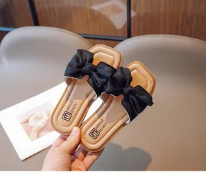Detail of children's beige slide sandals with a large black silk bow and branded footbed