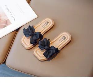 Detail of square-toe girl sandals featuring large black bow on beige leather base