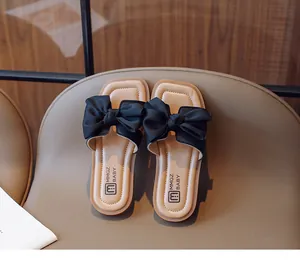 Detail view of children's black bow sandal featuring a soft beige sole on leather texture
