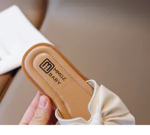 Close-up of baby girl mule shoes with cream bow and soft brown cushioned insole