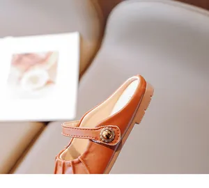 Close-up of caramel brown leather girl's mule shoes with golden embossed buckle