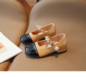 Detail of girls' khaki Mary Jane shoes featuring a black patent leather toe and pearl accent