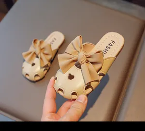 Dettaglio di ciabatte beige da bambina con fiocco grande e motivi a cuore traforati