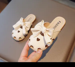Dettaglio di sabot da bambina in pelle beige con grande fiocco e cuori traforati