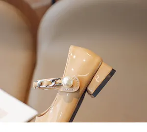 Detail of beige patent leather mary janes featuring silver chain and large pearl accent