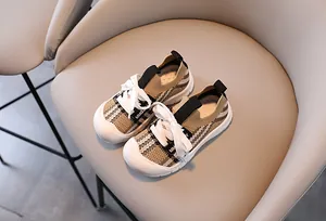 Detail of khaki plaid mesh kids sneakers with white rubber toe cap on a beige chair