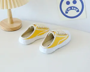 Close-up of bright yellow canvas mule sneakers on a white table with a cozy desk lamp