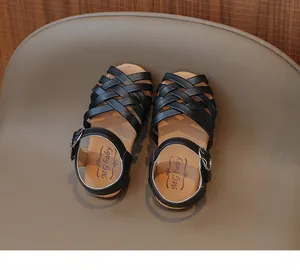 Détail de sandales noires tressées pour filles avec semelle souple et boucle métallique