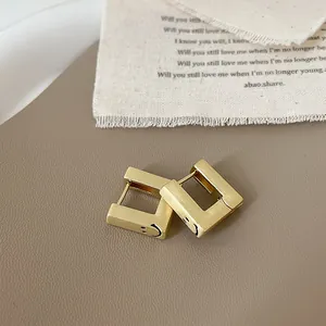 Gros plan de boucles d'oreilles carrées en or mat avec texture en métal brossé et sourire