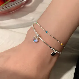 Detalle de tobillera doble de plata con un colgante de opalo colorido en forma de corazón