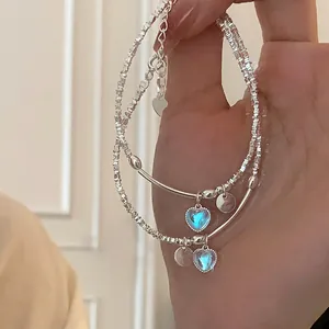 Detalle de pulsera plateada de doble capa con colgante de corazón azul y cadena fina
