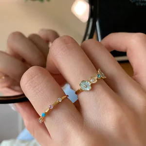 Close-up of elegant floral enamel rings and gemstone bands reflecting on a mirror surface